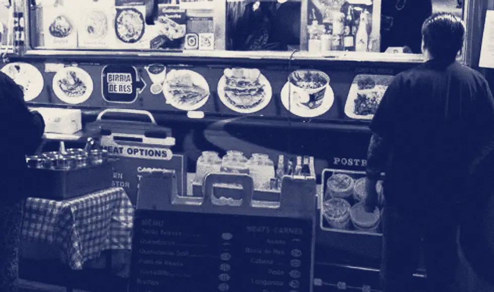 Two people order at the lit window of a food truck at night.
